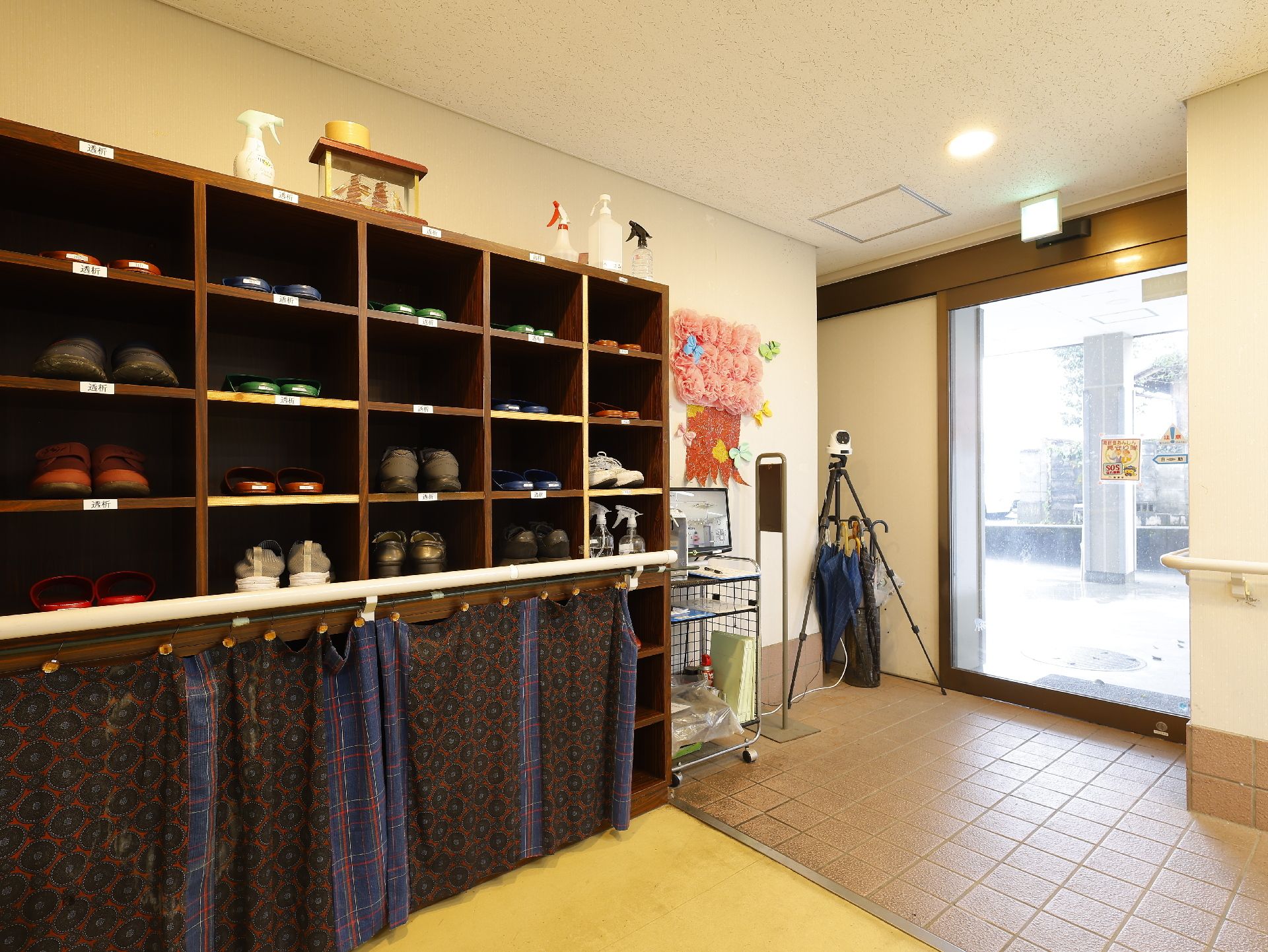 エプロンを付けた若い男女のスタッフに付き添われて屋外で楽しそうに過ごしている車いすの高齢女性と高齢男性。