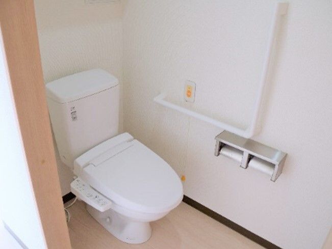 オレンジの呼び出しボタンや手すりが設置されたトイレ。温水便座が設置されたシンプルなデザイン。