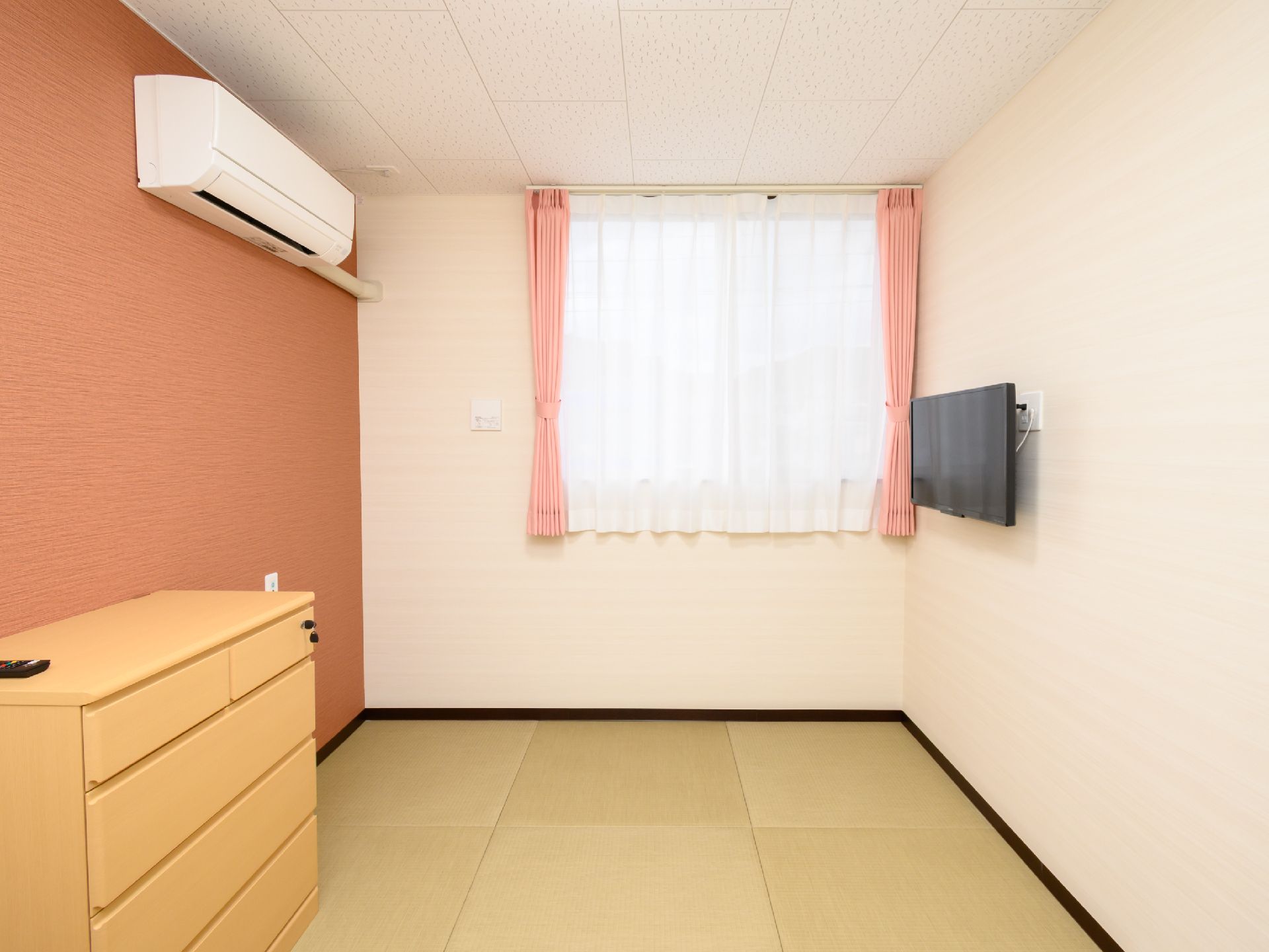 眼鏡をかけた高齢男性が車いすに座り、そばにいる白いゆったりとした服を着た高齢女性と笑顔で話している。