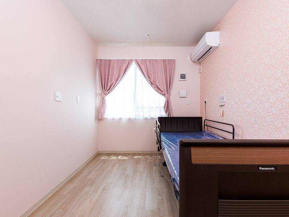 ピンク色を基調にした部屋の様子。介護用ベッドとエアコンが備え付けられている