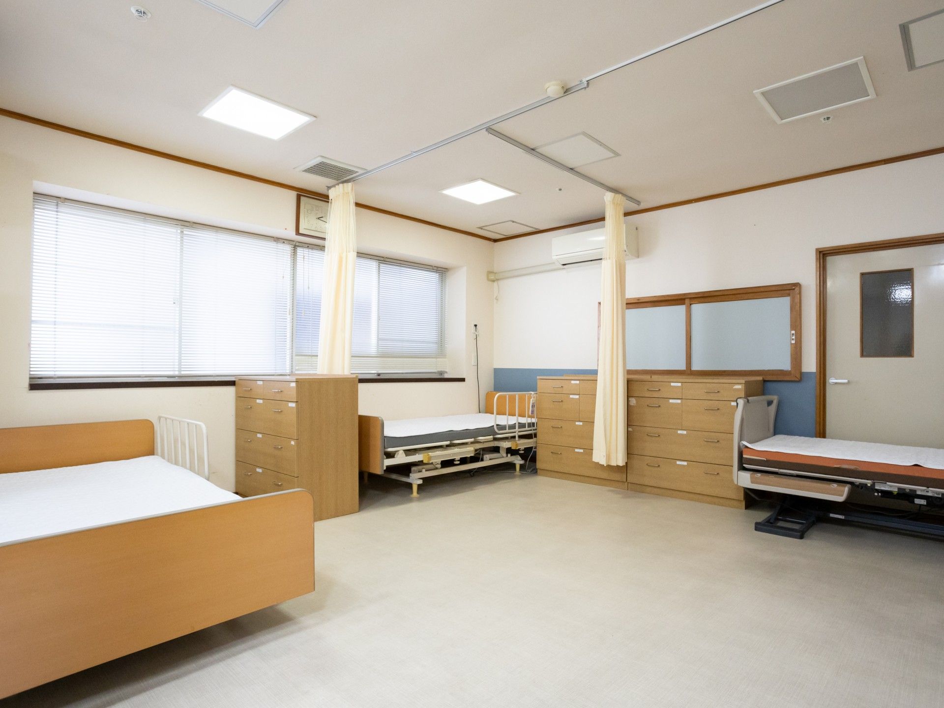 原っぱのような場所を散歩している高齢女性と付き添いのブルーのエプロンを付けた若い女性スタッフ。