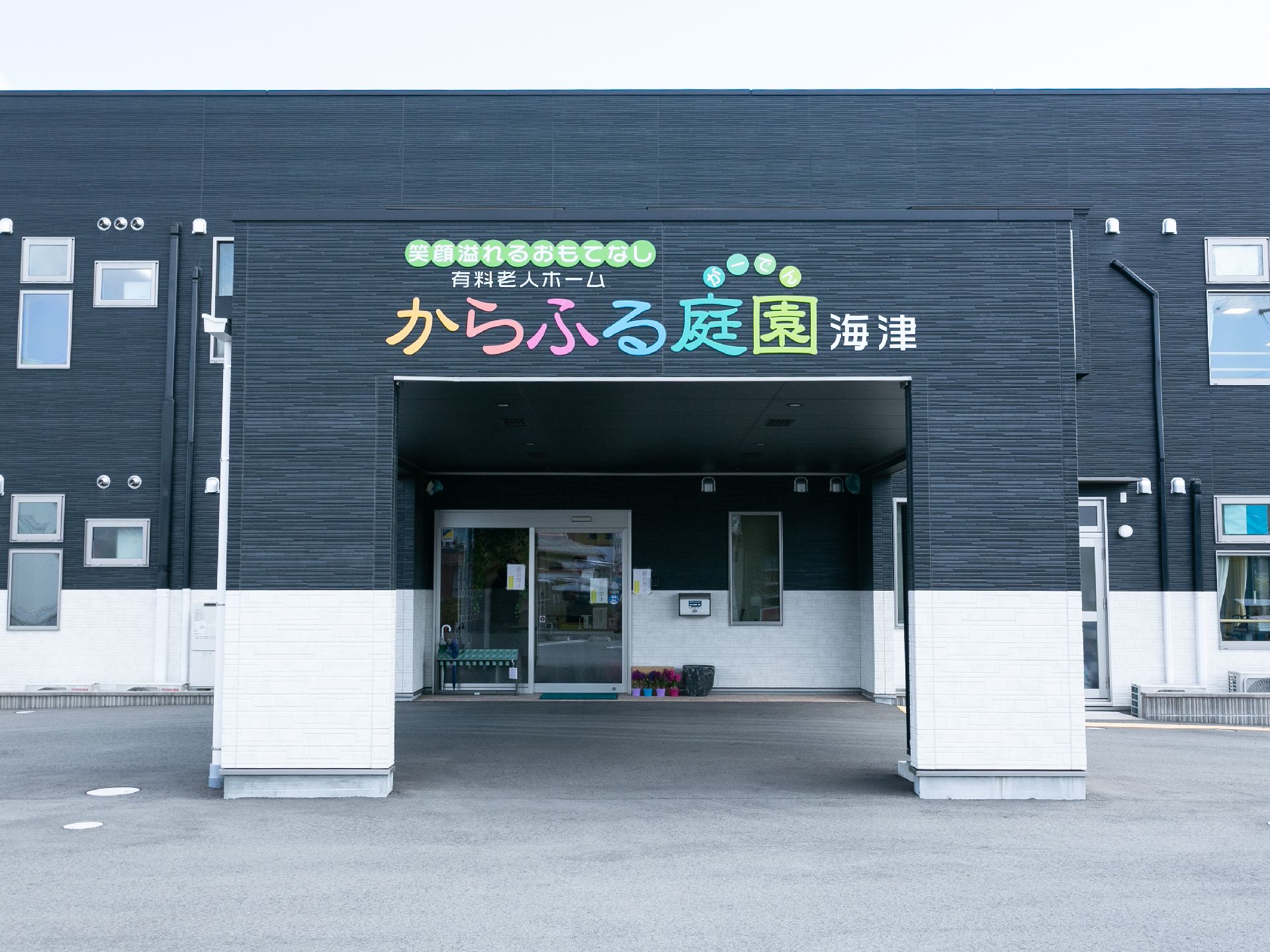 自然豊かな場所を車いすで散歩している高齢男性とそれを補助しながら話している女性スタッフ