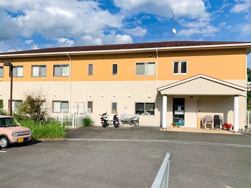 オレンジとベージュの2階建ての建物は横に長く、敷地内には広い駐車場があり、車が止められている。