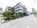 白黒の施設は角地に建っている。道路沿いには、植栽が植えられている。施設にはバイクを置くスペースもある。