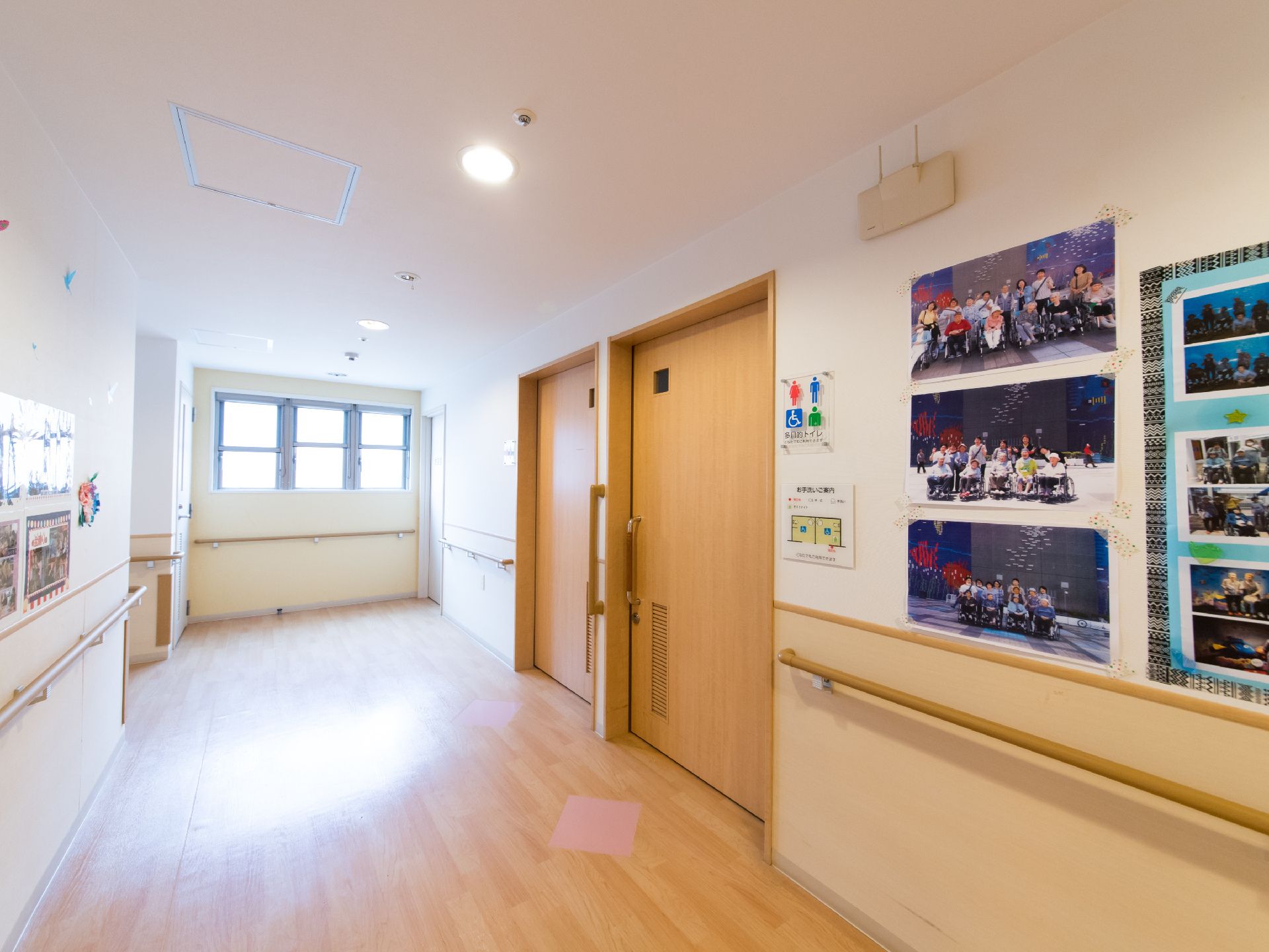 壁に複数の利用者の集合写真が掲示されている。トイレの横にはピクトグラムの表示がある。トイレのドアは引き戸。