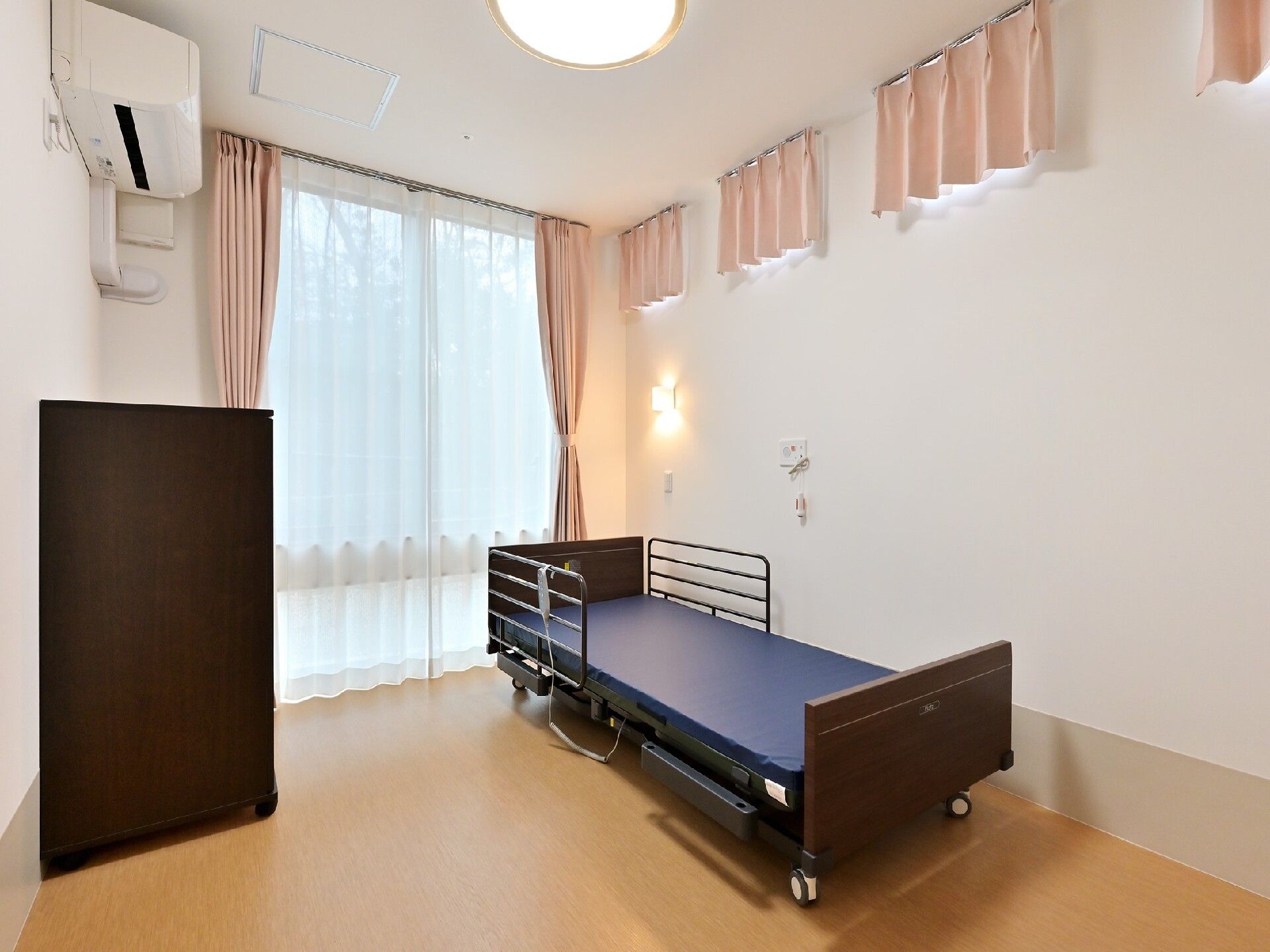 介護ベッドが置かれた部屋にはレースカーテンとカーテンが付いた窓があり、緊急通報装置やエアコンもある。