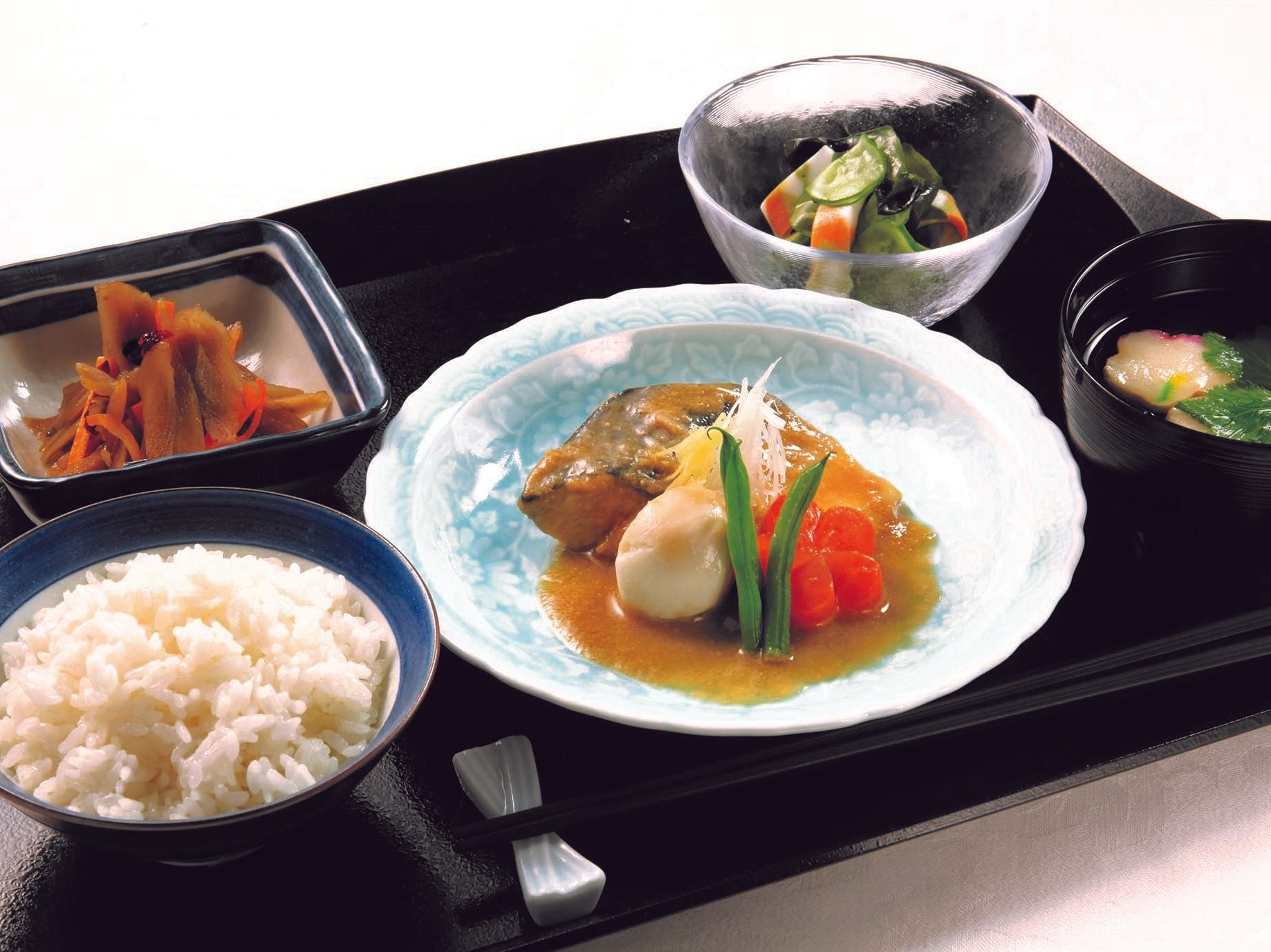 黒いトレーの上には白いご飯に汁物、酢の物やきんぴらなどが置かれ、中央にサバの味噌煮がある。