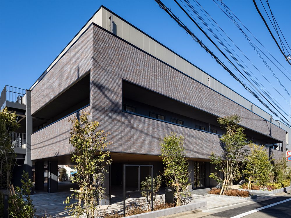 屋外階段が設置された3階建ての建物。横に長く、建物の周りには緑があり、落ち着いた色合いでまとめられている。