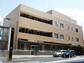 駐車場には数台の車が止まり、ブラウン系の３階建ての建物は重厚感があり、ベランダも付いている。