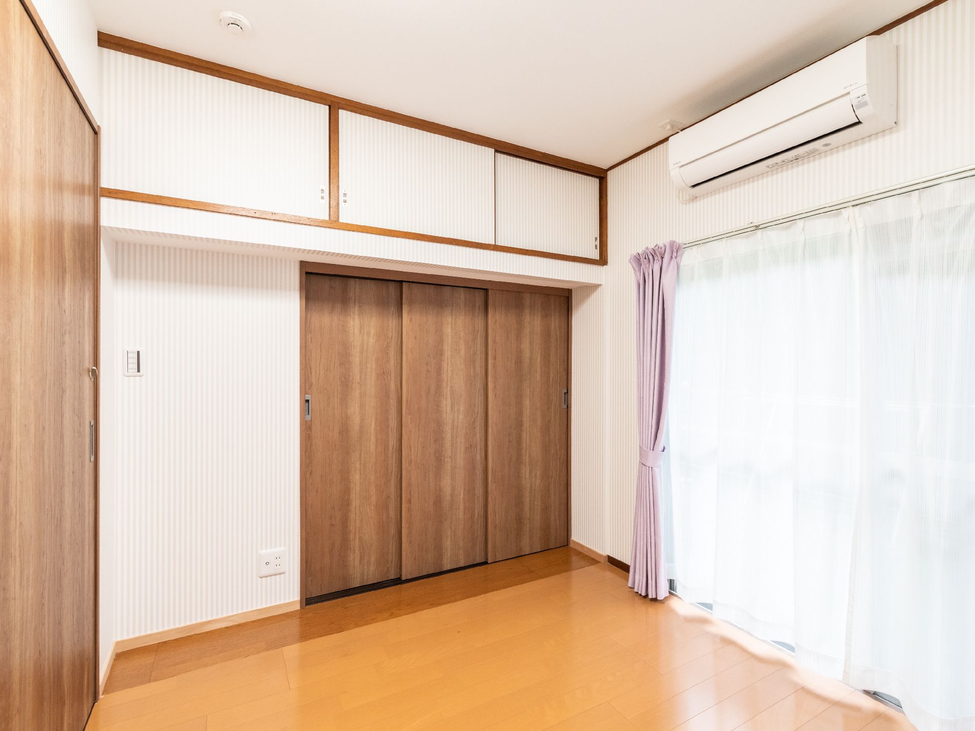 白いカーテンに遮られた窓とエアコンがある白い壁の部屋