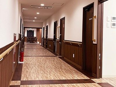 ブラウン系の色でまとめられた廊下。ベージュの手すりは縦横に設置され、居室のドアも両サイドにある。