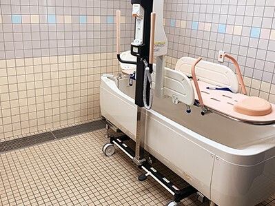 ピンクのストレッチャータイプのリフトが設置された機械浴。白い浴槽のような機械が壁際にある。