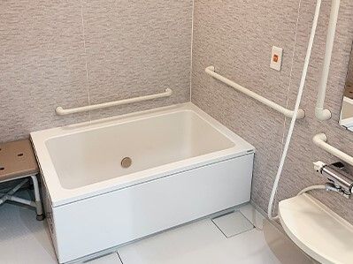 オレンジの呼び出しボタンや手すりが付いた一人用の浴槽。浴槽のそばにはベンチがある。