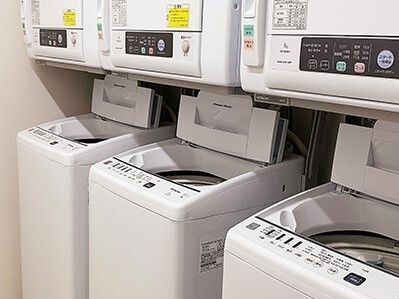 縦型の洗濯機の上に乾燥機が設置されたセットが3組あり、それぞれの洗濯機のふたは開けられている。