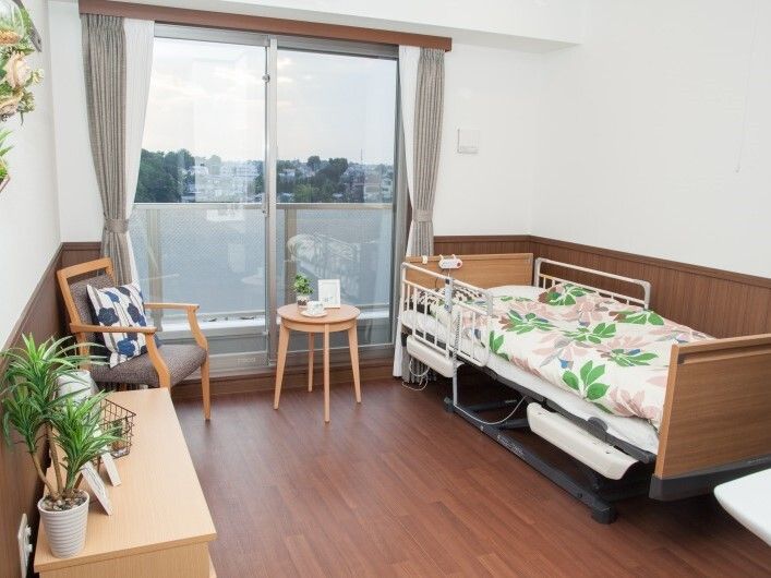 エプロンを付けた若い男女のスタッフが車いすの高齢の男女に付き添い、屋外で過ごしている様子。