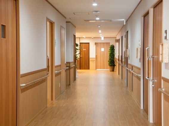 幅の広い廊下の両サイドに手すりと居室のドアがあり、奥には観葉植物が置かれた共有スペースがある。