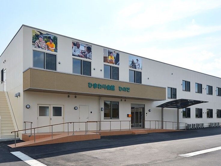 手すり付きのスロープや屋外階段が付いた2階建ての建物。2階部分の外壁にはヒマワリの絵が描かれている。