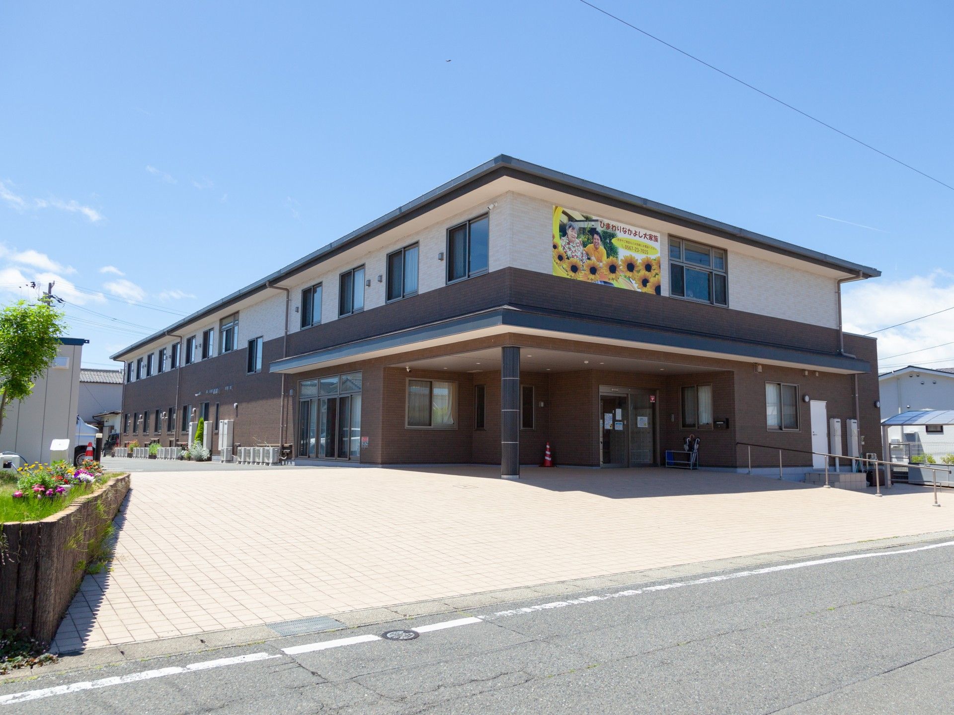 2階建ての建物は1階部分がダークグレー、2階部分が白で、外壁にはヒマワリの絵が描かれ、車寄せもある。