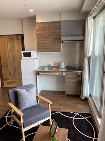 車いす対応のキッチンが付いたフローリングの部屋にはいすやテーブルがあり、ラグも敷かれている。