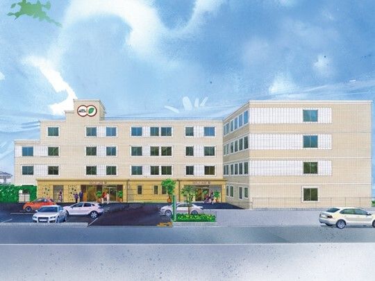 4階建ての建物の外壁はベージュで敷地内には駐車場があり、車が止まっている。