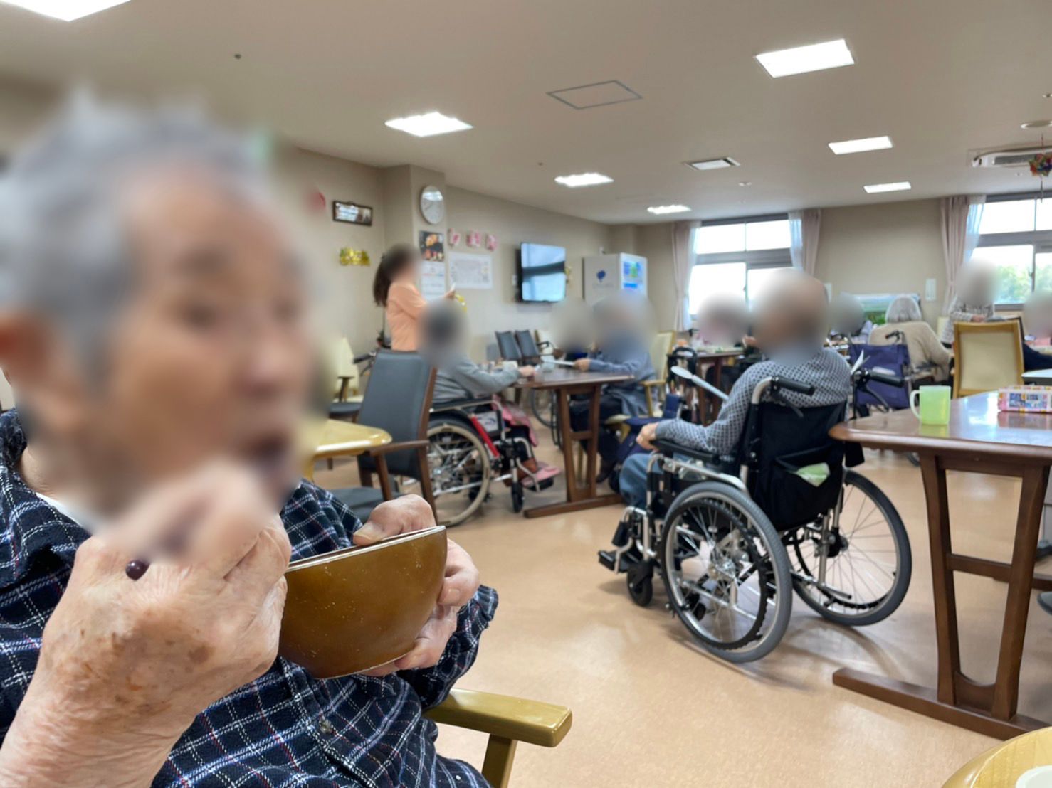 奥ではスタッフと入居者がレクリエーションを楽しんでいる。手前の席では男性が食事をしている。