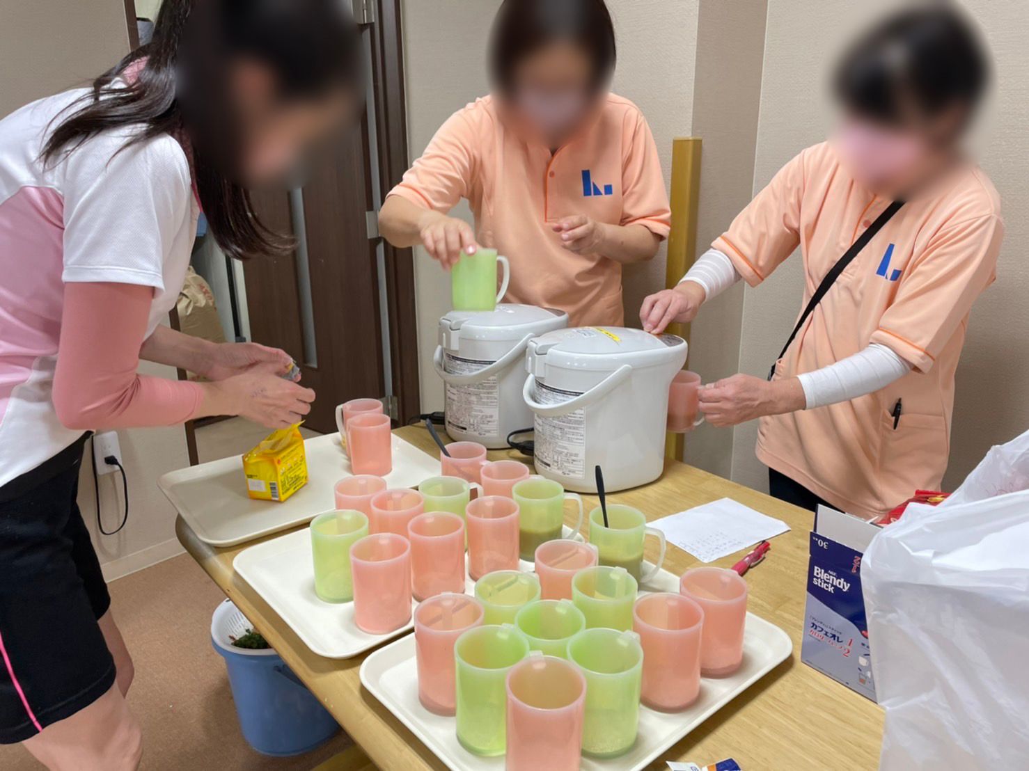 グリーンやピンクのプラスチック製のコップに飲み物を入れている数名の女性スタッフ。