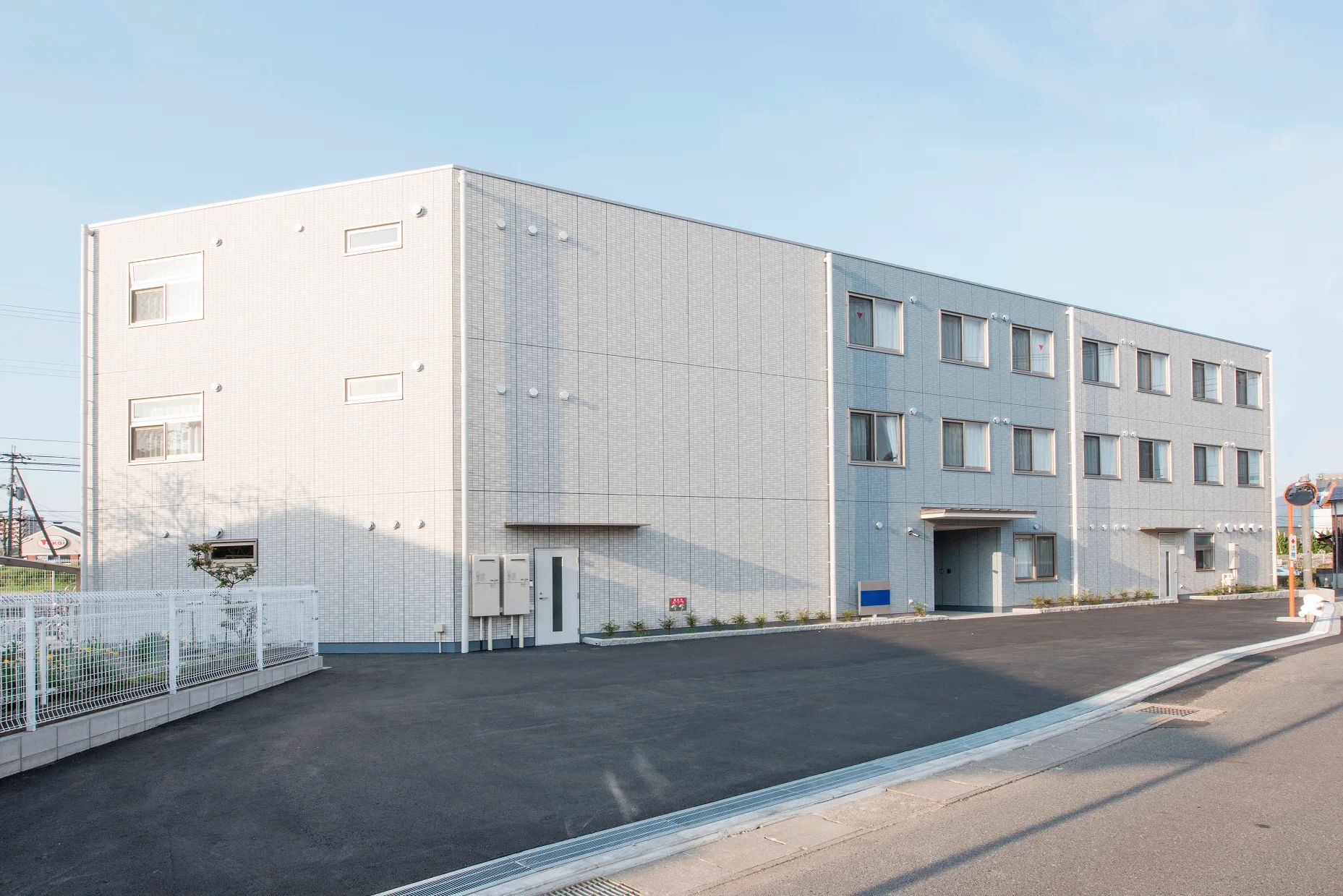 ブルーがかかったグレーの外壁の3階建ての建物は玄関に小さな屋根が付き、窓もたくさん付いている。