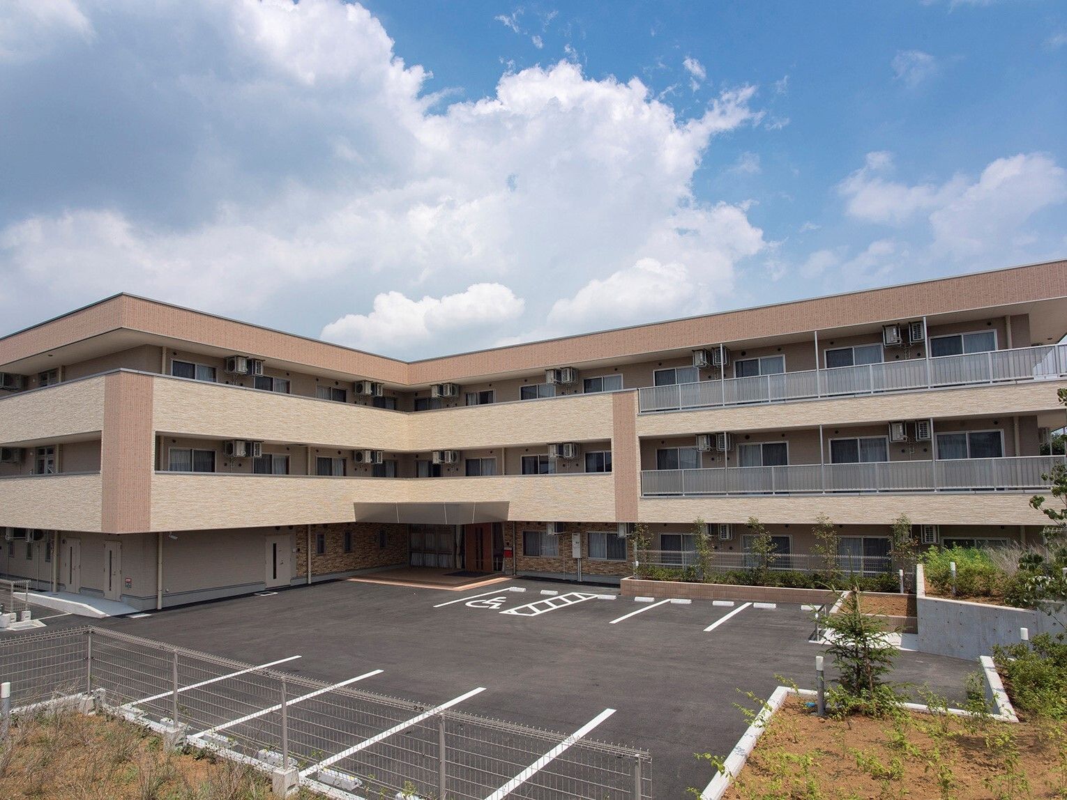 エル字型の３階建ての建物は各フロアにベランダがあり、広い駐車場が付いている。ベージュとブラウン。