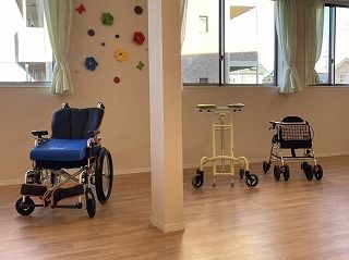 手作りの飾りが飾られた共有スペースには青い車いすや歩行器、シルバーカーが並べられている。