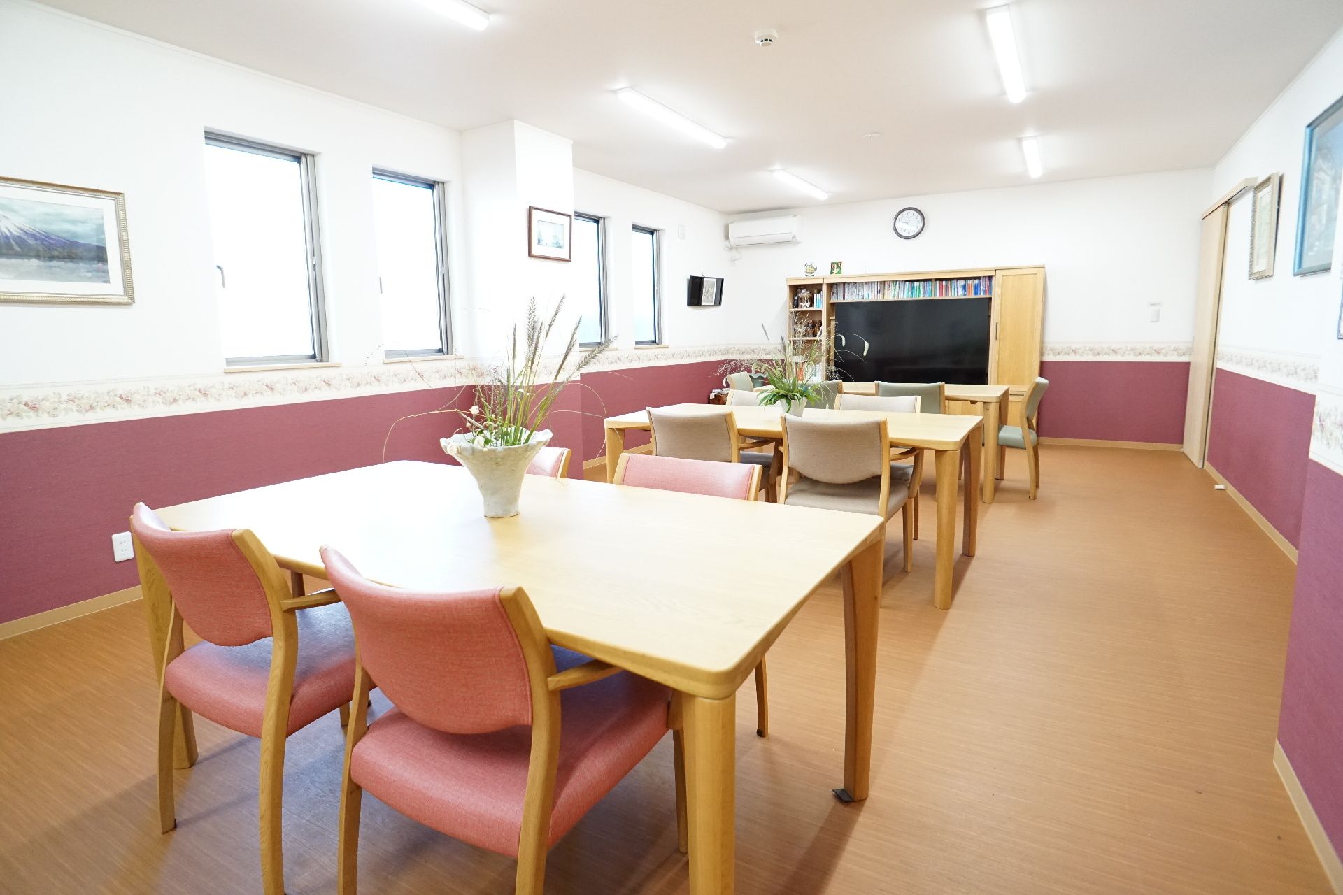 カルテのようなものを持って笑顔で話しているピンクのポロシャツを着た女性スタッフと白髪の高齢女性。