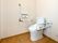エル字型の手すりと可動式の手すりが両サイドに付いた広いトイレ。トイレットペーパーホルダーは二連式のものが付いている。