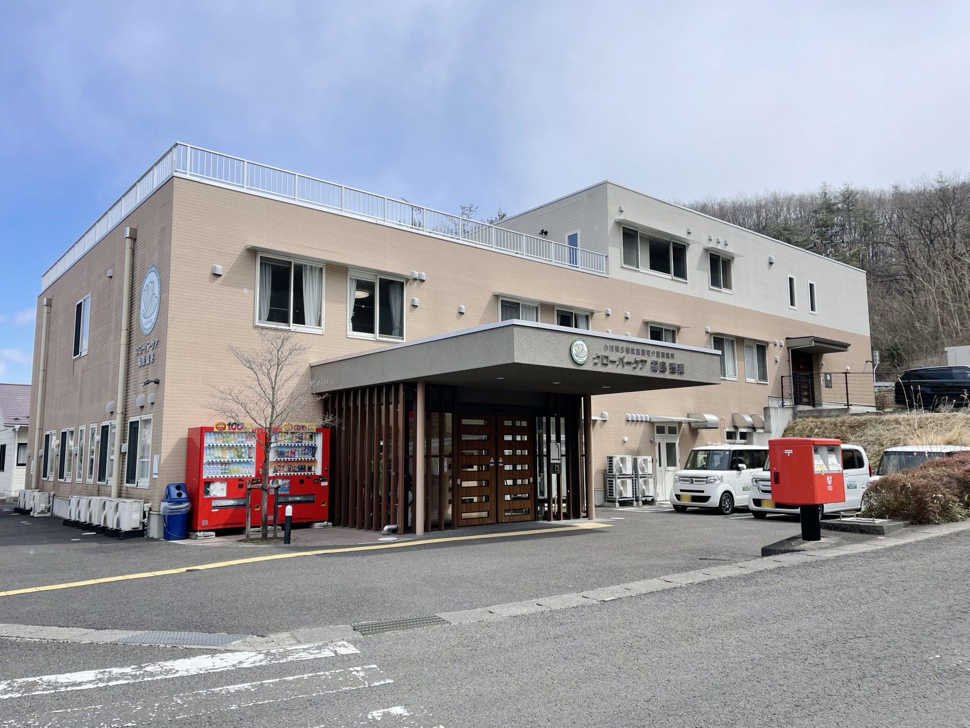 ブルーのエプロンを付けた若い女性スタッフに付き添われて屋外で過ごしている車いすの高齢女性。