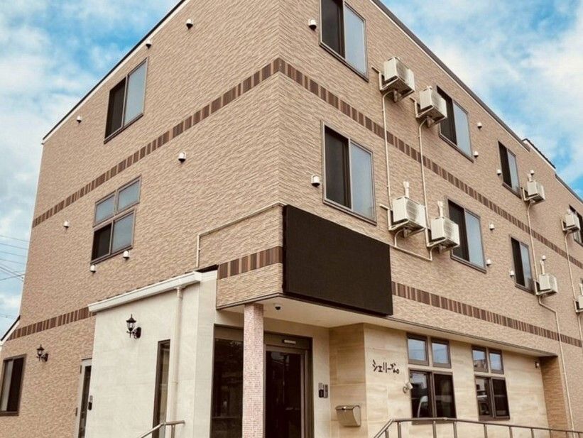 レンガ調の外壁の３階建ての建物の玄関には屋根と手すり付きのスロープが設置されている。