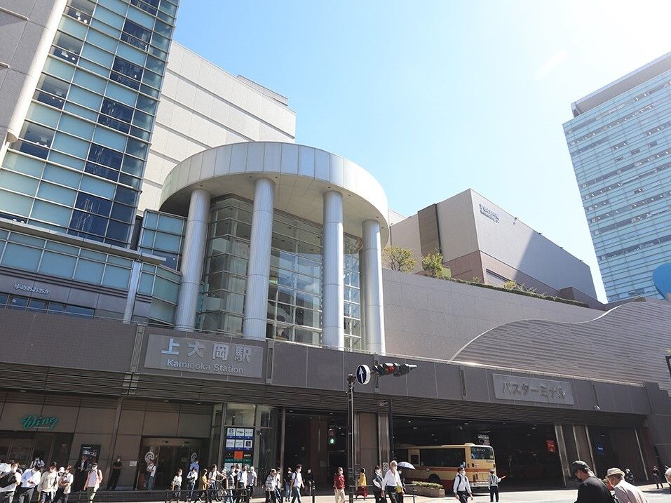 人通りの多い駅前の様子。周りには背の高いビルが建ち並び、駅の奥には黄色いバスも止まっている。