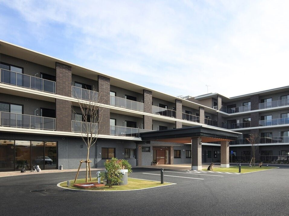各フロアにベランダが付いたブラウン系の３階建ての建物が建っている敷地内には駐車場がある。