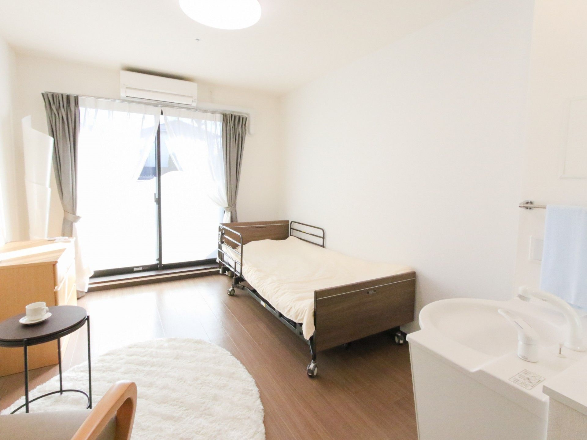 大きな窓が付いているフローリングの部屋には観葉植物があり、タンスや一人用の椅子が置かれている。