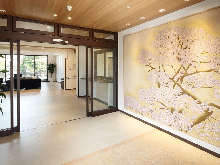 段差のないエントランスの壁にはやわらかい光に包まれた桜の絵が描かれ、奥にはソファが設置されている。