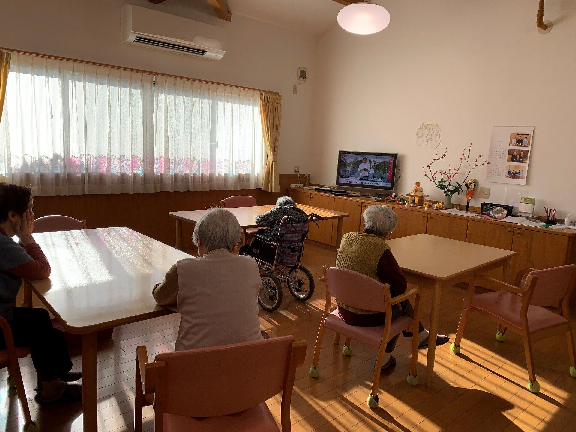 車いすに乗る高齢者が笑顔で手を振っている様子と車いすを押している介護スタッフ