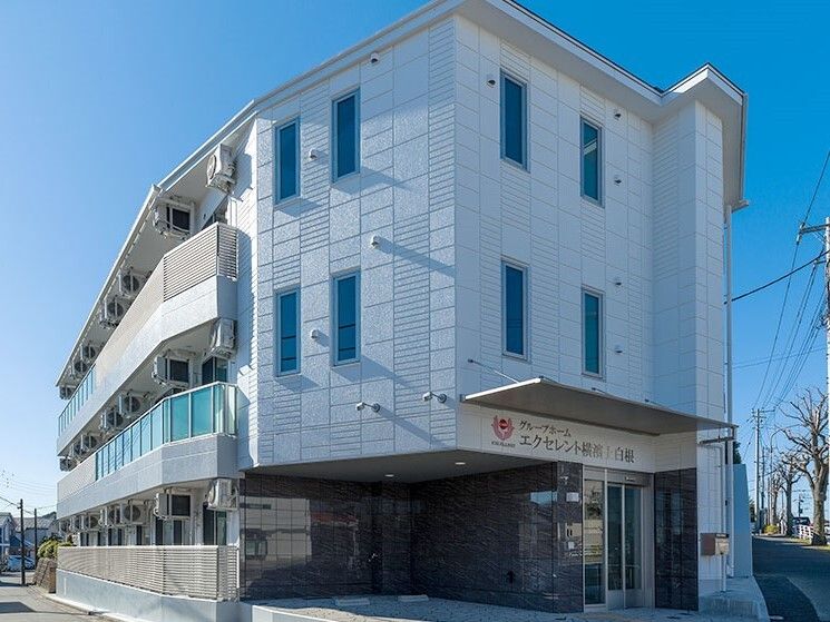 ライトブルーの3階建ての建物は日当たりのいい場所に建っていて、玄関には屋根が付いている。