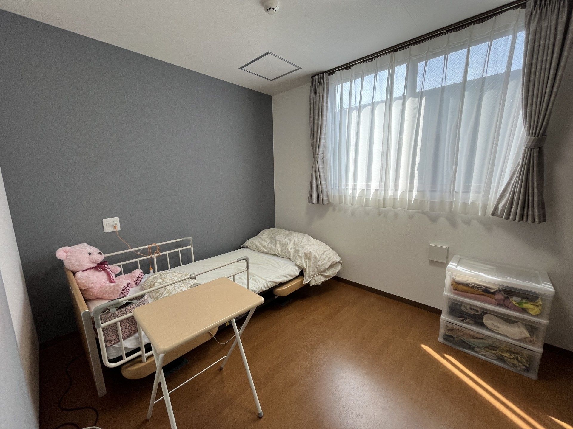 薬を飲もうとしている高齢女性のそばにはピンクのエプロンを付けた若い女性スタッフがいて、微笑みながら水の入ったコップを持っている。