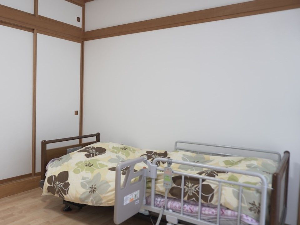 高齢者2名とスタッフが手を握りながら談笑している様子。施設内の会話の一画面