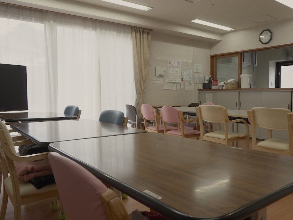 高齢者の方にタオルをかけてマッサージしているスタッフと振り返りながら会話する女性の様子