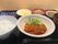 オニオンソースがかかった魚料理をメインとして、白いご飯に味噌汁、シバ漬け、カットフルーツ、野菜の和え物やせんべいがある。