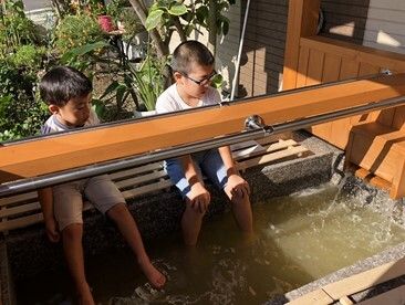 足湯を楽しんでいる２名の男児。足湯の中央には手すりが設置され、二人は並んで座っている。