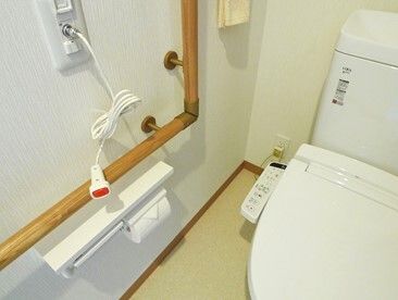 赤いプッシュ式の呼び出しボタンが設置されたトイレには木製のエル字型の手すりが設置されている。