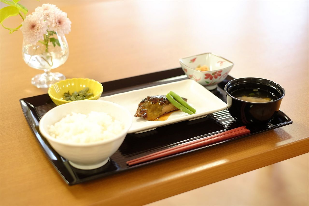 トレーの上には魚料理や白いご飯、みそ汁、野菜の小鉢が数品などが並べられている。