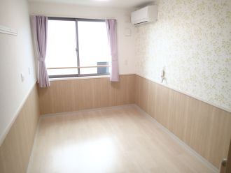 エアコンが付いたフローリングの部屋には花柄の壁紙が貼られ、緊急通報装置も付いている。