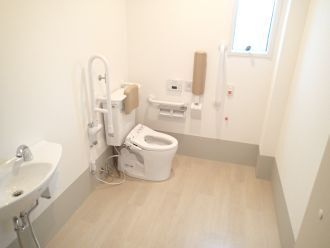 ふたのない便座には手すりや背もたれが付き、壁にはバーもある。介助スペースが広く、手洗い場もある。