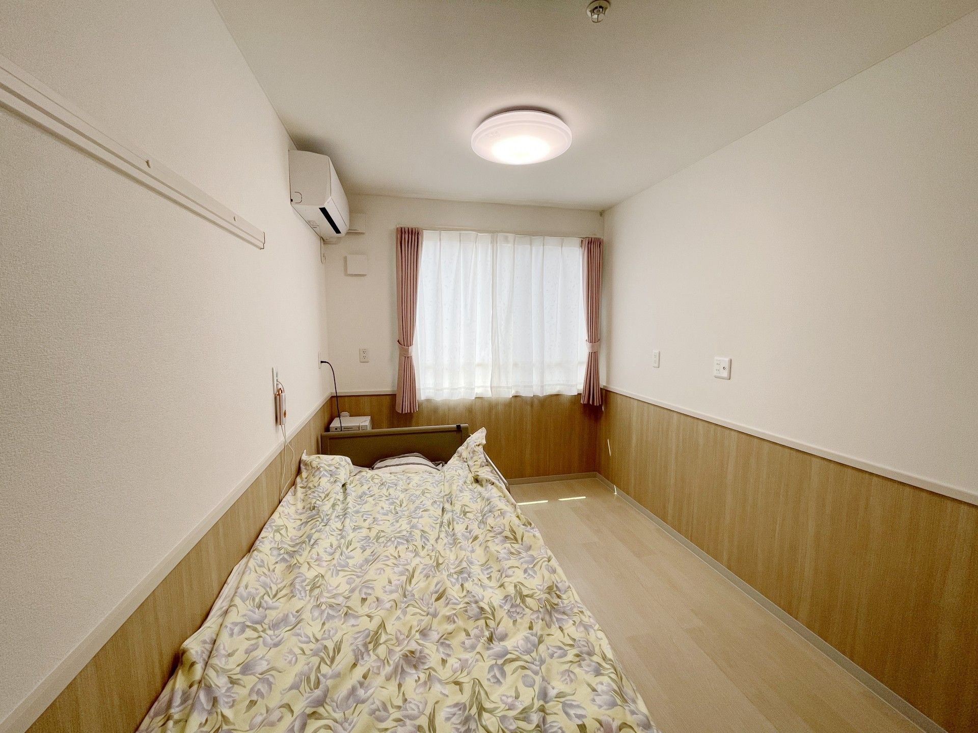カーテンが付いた大きな窓があるフローリングの部屋には、緊急通報装置やエアコンも設置されている。