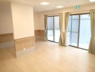 大きな窓にはベージュのカーテンが付き、壁には手すりが付いている。フローリングのフロアには何も置かれていない。